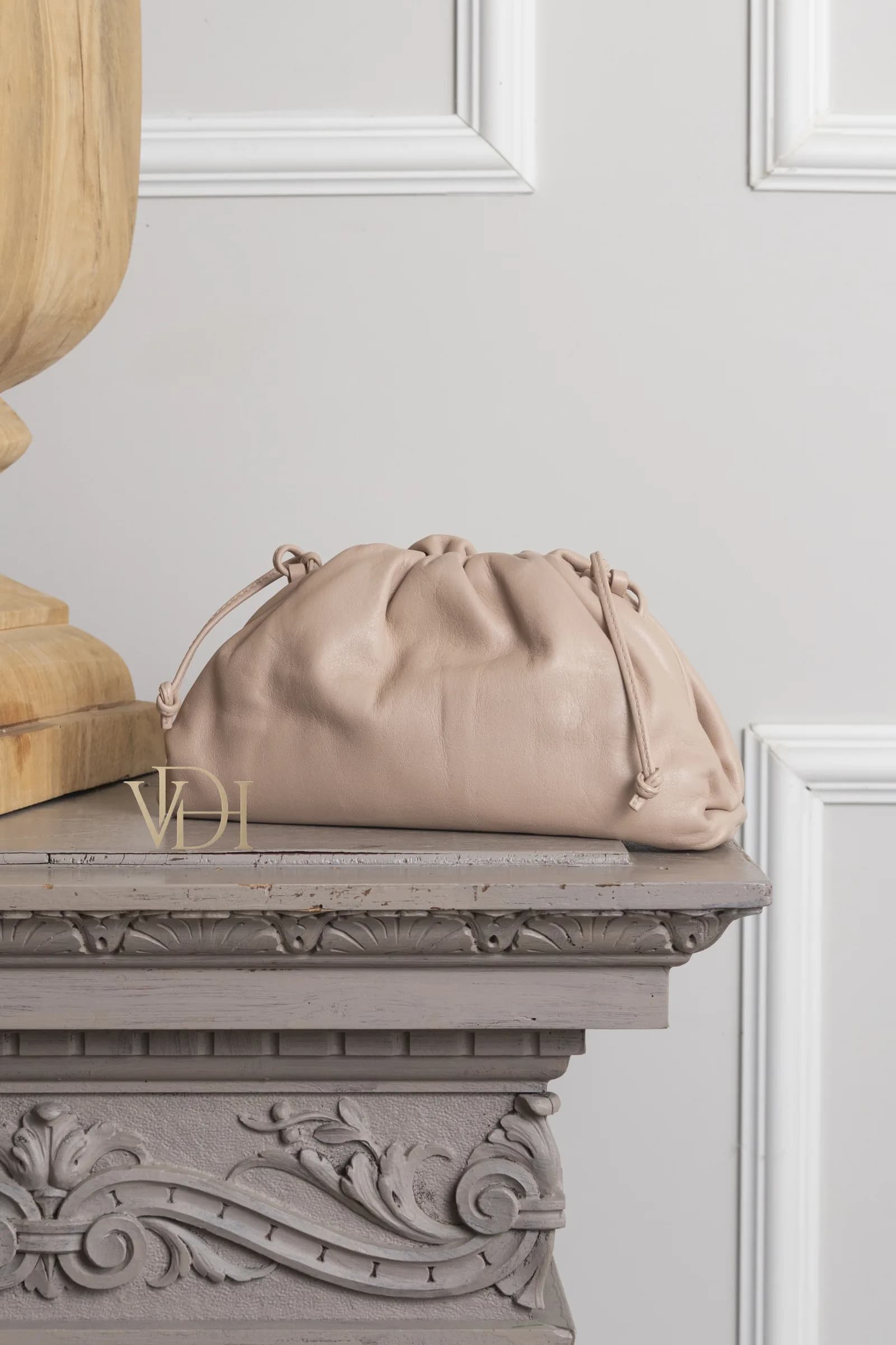 Bottega Veneta Pouch color nude sul camino di marmo grigio, colonnetta in legno chiaro — ambiente editoriale curato